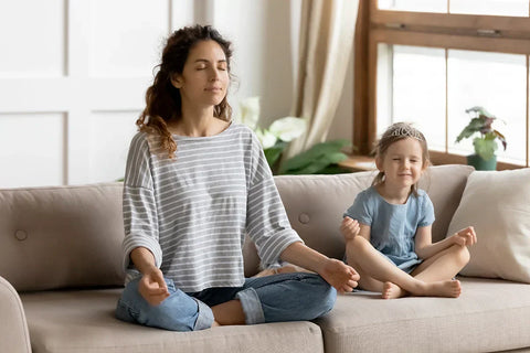Mother and young daughter doing breathing excercises on a taupe couch