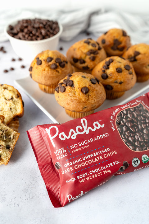 Chocolate chip muffins rest on a white rectangular plate on a grey speckled surface with a 100% dark chocolate chip bag resting in front and a white bowl full of chocolate chips rests behind.