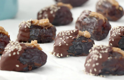 Close up image of half dipped dates with sesame seeds sprinkled