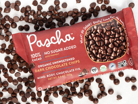 A bag of Pascha's 100% No Sugar Added Chocolate Chips bag with the corner cut off and the chocolate chips all laid out surrounding the bag