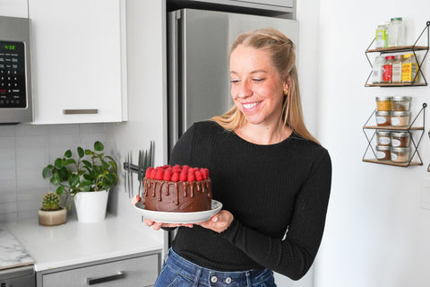 Smiling blonde lady looking at chocolate cake topped with fresh raspberries.
