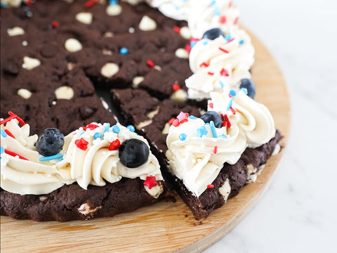 Slice of a triple chocolate cookie with a vegan white chocolate cream cheese icing and decorated with patriotic sprinkles.