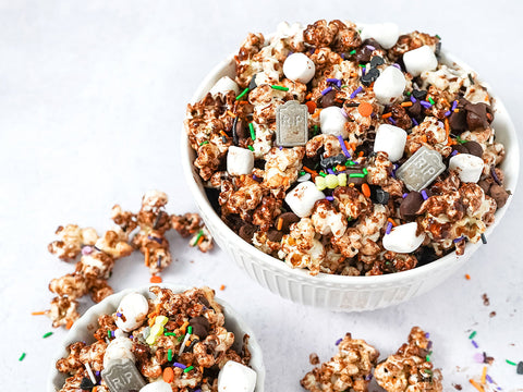 A bowl of halloween popcorn which consists of popcorn covered in dark chocolate with sprinkles and vegan small marshmallows.