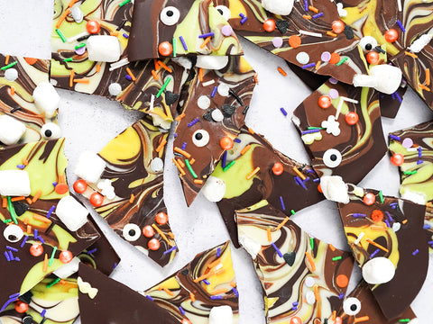 Monster Mash halloween bark made up of dark chocolate, green dyed white chocolate and swirled around with coloured sprinkles. The chocolate bark is cut up into various sized pieces.
