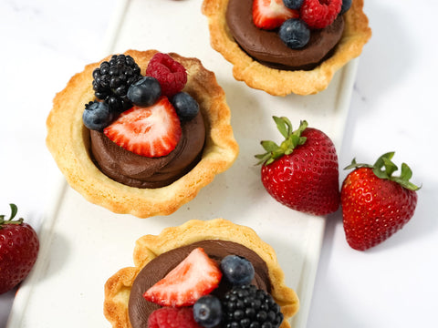 Three chocolate mousse cookie cups with a variation of berries resting on top of each one and two whole strawberries laying beside the cookie cups