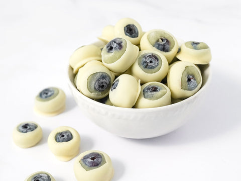 Blueberries covered in white chocolate so that they look like eyes resting in a white bowl with a few laying beside the bowl