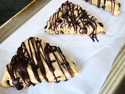 Cranberry scones on a baking sheet drizzled with melted dark chocolate.