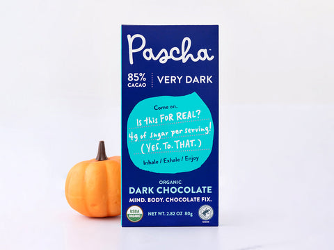 Pascha's 85% Very Dark Chocolate Bar is standing upright with a small orange pumpkin just slightly behind the bar