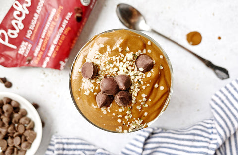 Vegan chocolate smoothie in a clear glass topped off with hemp seeds and chocolate chips.