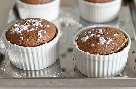 Four chocolate souffles in ramekins on a baking sheet and sprinkled with icing sugar.