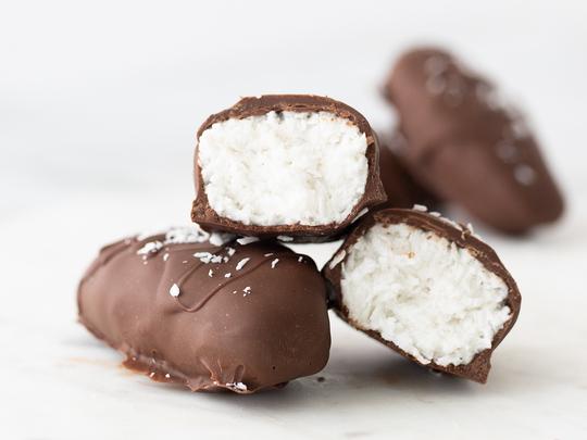 Chocolate bounties stacked on top of each other, one of them is cut in half so you can see the white coconut filled inside.