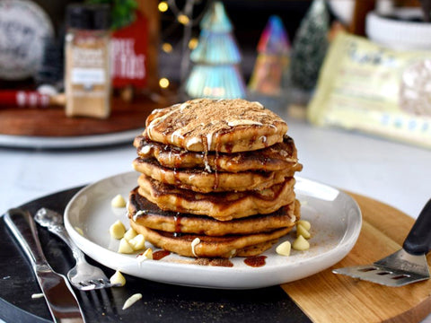 Stack of pancakes on a white plate drizzled with syrup and white chocolate and sprinkled with white chocolate chips.