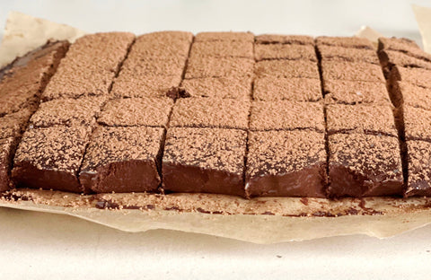 chocolate coffee nama truffles cut into squares and sprinkled with cocoa powder on a piece of parchment on a white counter
