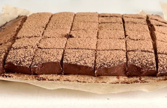 chocolate coffee nama truffles cut into squares and sprinkled with cocoa powder on a piece of parchment on a white counter