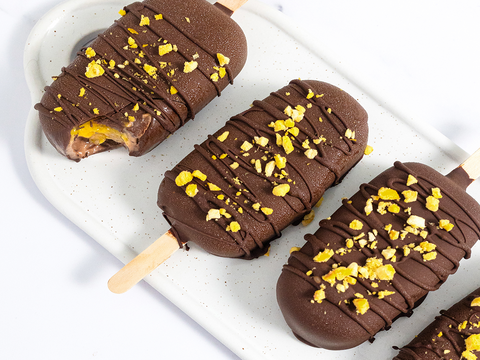 Vegan Mango Jam Protein Fudgsicles are laying on a white plate and one of them has a bite bitten out of it.