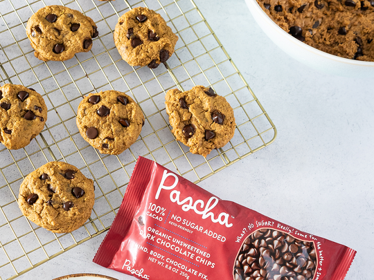 Ginger Chocolate Chip Cookies on a cooling rack with a bag of Pascha's 100% Dark Chocolate Chips laying beside.