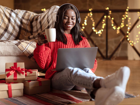 Woman listening to music on headphones while smiling with christmas decor in the background