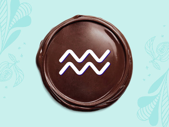 White Aquarius sign on a disc of melted dark chocolate on a light teal background.