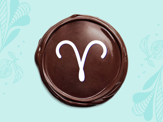 White Aries sign on a disc of melted dark chocolate on a light teal background.