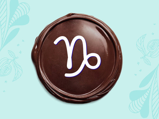 White Capricorn sign on a disc of melted dark chocolate on a light teal background.
