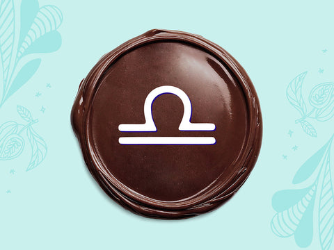 White Libra sign on a disc of melted dark chocolate on a light teal background.