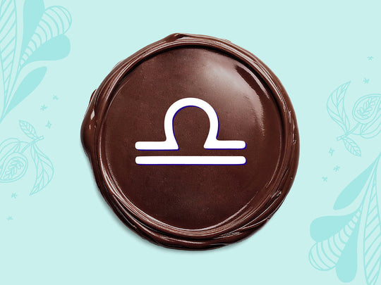 White Libra sign on a disc of melted dark chocolate on a light teal background.