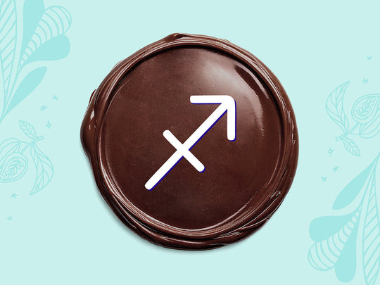 White Sagittarius sign on a disc of melted dark chocolate on a light teal background.