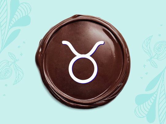 White Taurus sign on a disc of melted dark chocolate on a light teal background.