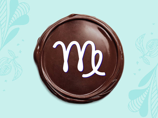 White Virgo sign on a disc of melted dark chocolate on a light teal background.