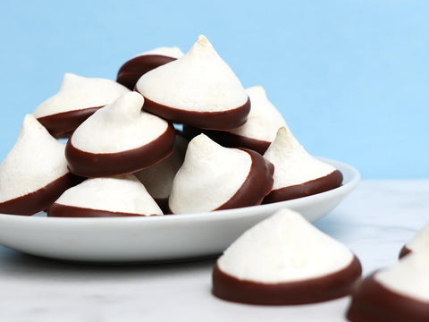 White plate on a white counter filled with meringue cookies dipped in chocolate.