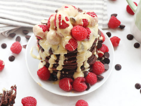 Stack of Chocolate Banana Pancakes topped with raspberries and melted white chocolate.