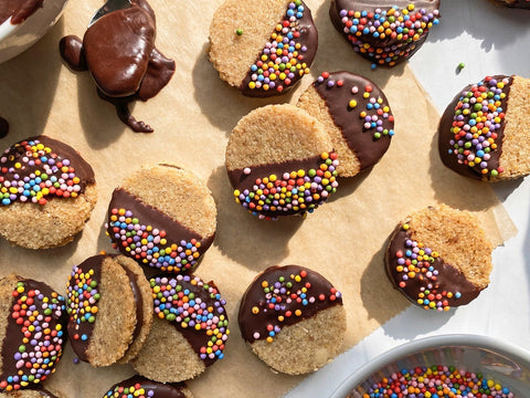 Pile of sandwich cookies dipped in chocolate and sprinkles.