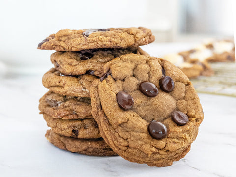 Bright photo of stack of chocolate chip cookies with melty chocolate chips on them on a white marble surface.