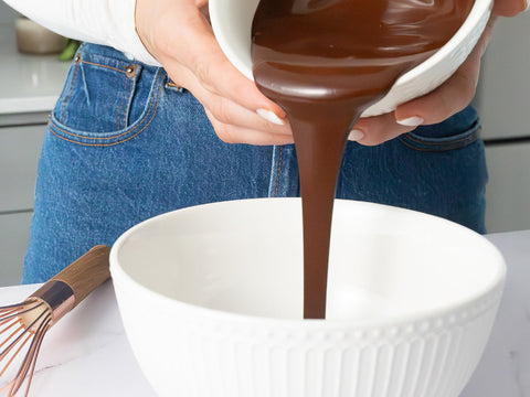 hands holding white bowl of melted chocolate pouring into a bigger white bowl