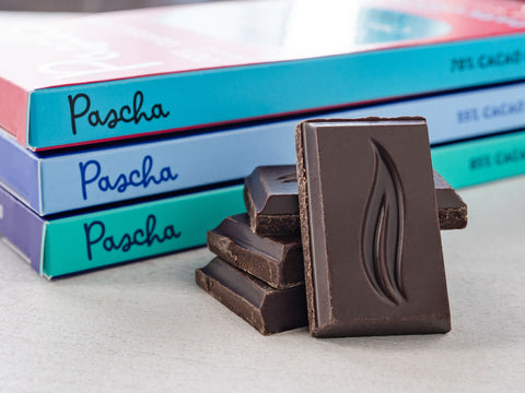 Three Pascha Chocolate bars laying down and stacked on top of each other with a pile of broken bar pieces in the fore front.