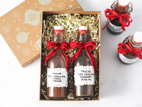 Gift box filled with gold crinkle paper and two bottles of Pascha chocolate infused oils with red ribbon tied around their necks.