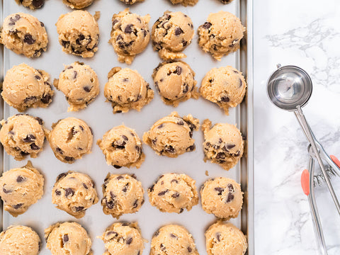 Peanut Butter Chocolate Chip Cookie Dough lined on a baking sheet with parchment paper with a cookie scooper beside on the table 