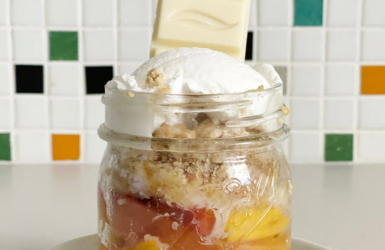 small mason jar with peach cobbler topped with vanilla ice cream and a chunk of Pascha vegan white chocolate