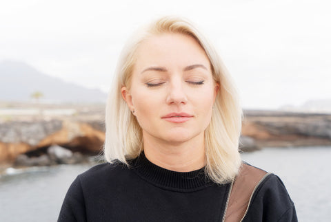Blonde woman standing with eyes close taking a quiet moment