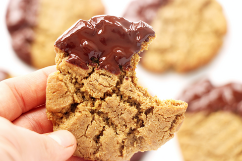 Hand holding cookie dipped in melted chocolate and a bite out of it with more cookies dipped in chocolate in the background