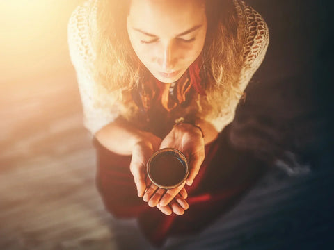 Woman with eyes closed holding a cup of cocoa in dim room