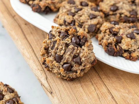 Oatmeal chocolate chip cookie leaned against white plate full of cookies on wood board
