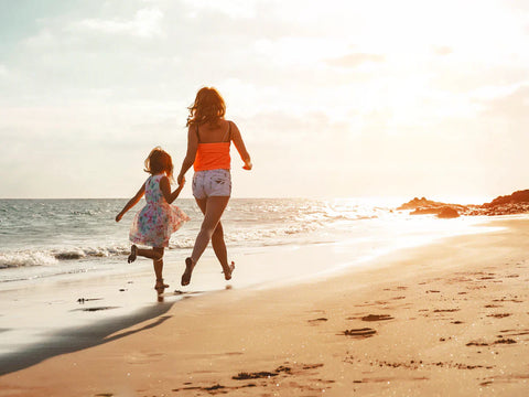 Mother and daughter running down beach at sunset