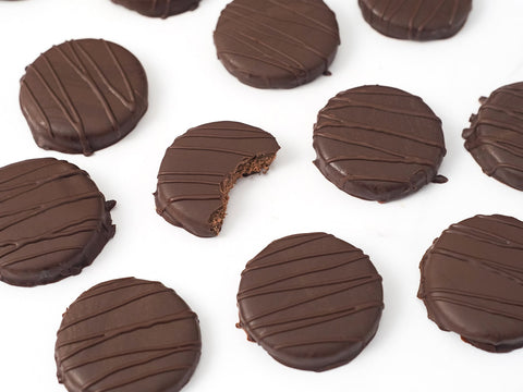 Thin mints drizzled with chocolate on a marble counter and one bite taken out of one.