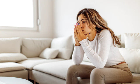 Long haired woman with head resting hands sitting on a couch looking melancholy