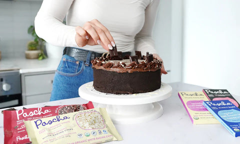 Woman in jeans and white shirt placing piece of chocolate on a chocolate cake