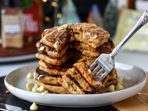 Stack of pancakes sprinkled with white chocolate chips on a white plate with a fork holding a bite.