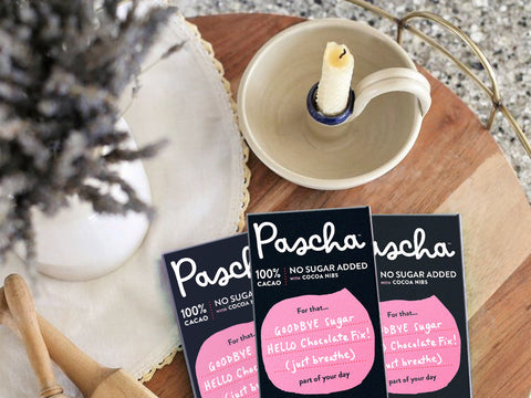 Pascha 100% bars on a small round wood table with lavender in a vase and a candle.