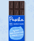 The front of Pascha Chocolate's 55% with Barely Dark Chocolate Bar with half of the exposed bar sticking out of the top of the packaging