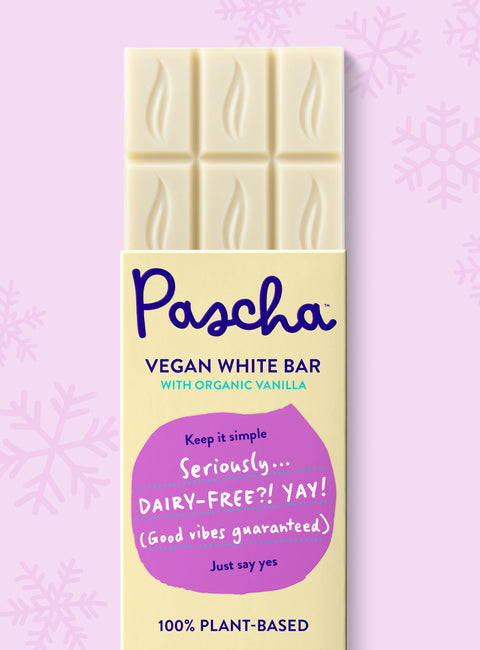 The front of Pascha Chocolate's Vegan White Bar with half of the exposed bar sticking out of the top of the packaging on a light pink background with subtle snowflakes.